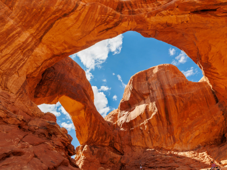 The image shows a natural rock arch with a vivid blue sky in the background, featuring rugged red rock formations and contrasting textures.