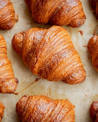 Golden-brown croissants arranged neatly on a baking sheet.