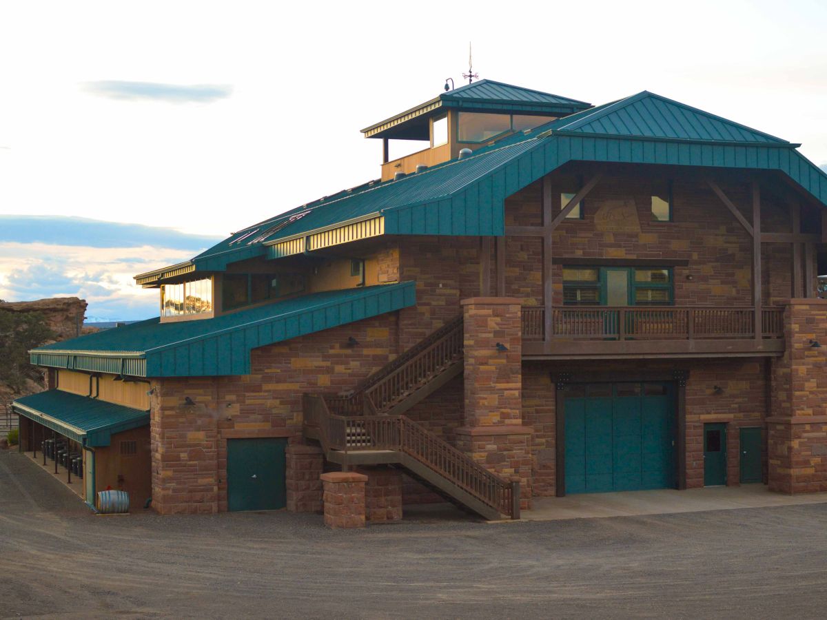 A multi-level building with stone walls and teal roofs, featuring exterior staircases and set in a spacious open area.
