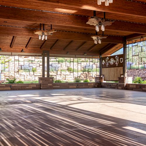 An open wooden pavilion with large windows, light fixtures, and a view of greenery outside.