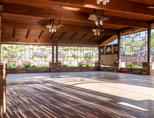 An open wooden pavilion with large windows, light fixtures, and a view of greenery outside.