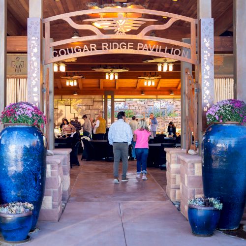 An entrance to a pavilion with large blue planters and two people walking inside.