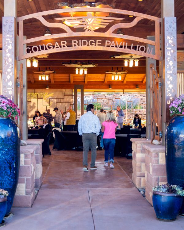 An entrance to a pavilion with large blue planters and two people walking inside.