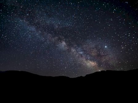 A starry night sky featuring the Milky Way galaxy, with silhouetted hills in the foreground.
