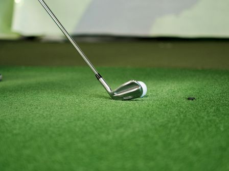 A golf club poised above an artificial green surface with a shadow in the background.