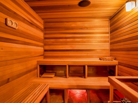 The image shows a wooden sauna interior with benches, lighting, and a warm ambiance, creating a cozy and relaxing environment.