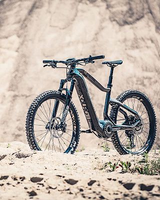 The image shows a mountain bike with knobby tires and sleek design, set against a rocky outdoor backdrop.