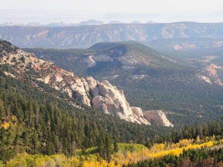 A scenic view of a mountainous landscape with dense forests, rocky outcrops, and a mix of green and yellow foliage covering the hillsides.