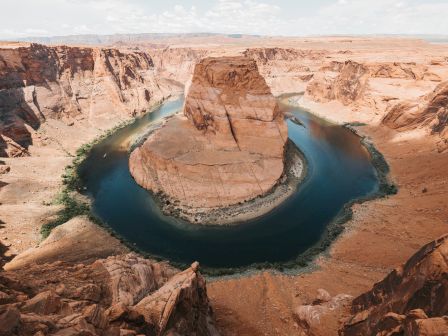 A horseshoe-shaped meander with a river flowing around a rock formation, set in a desert landscape under a clear sky.