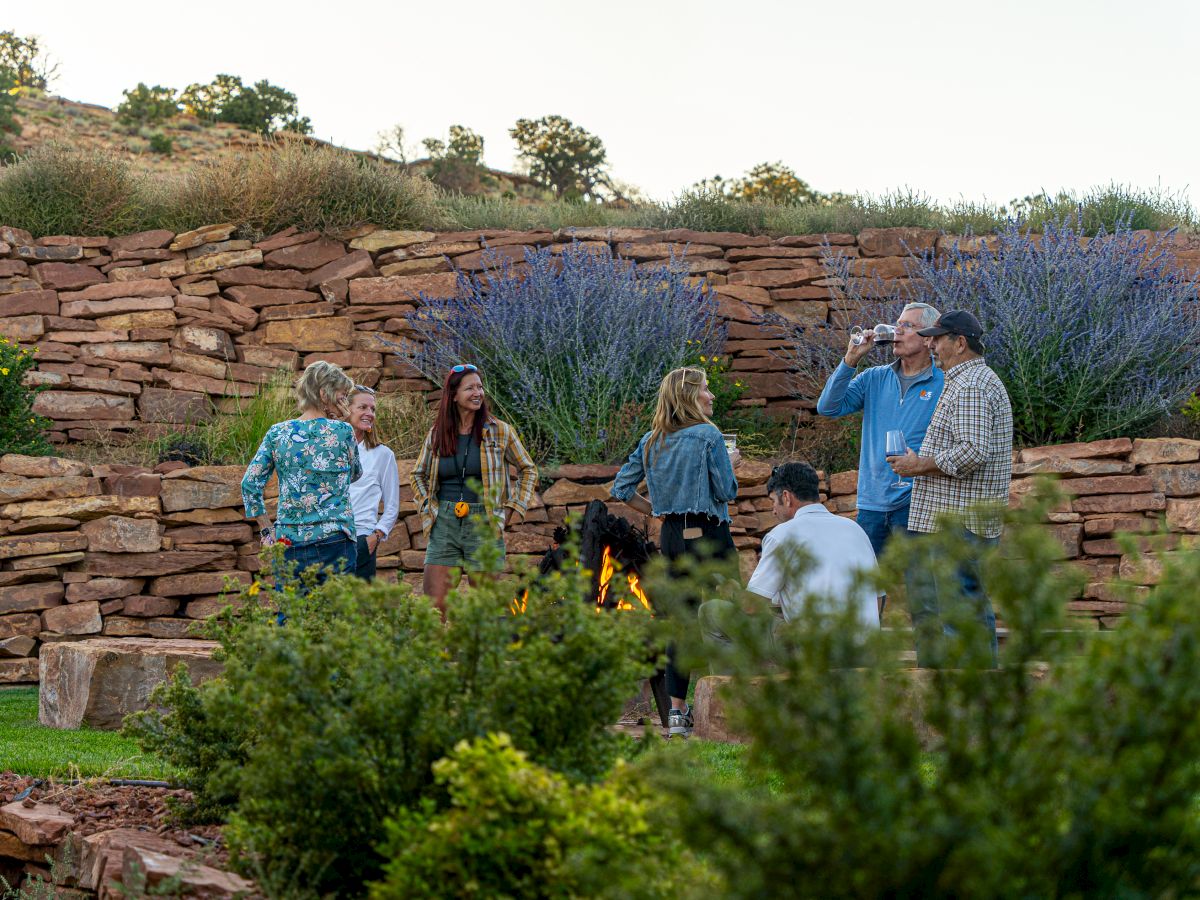 A group of people gathered outdoors in a garden setting with stone walls and lavender plants, possibly engaged in conversation.