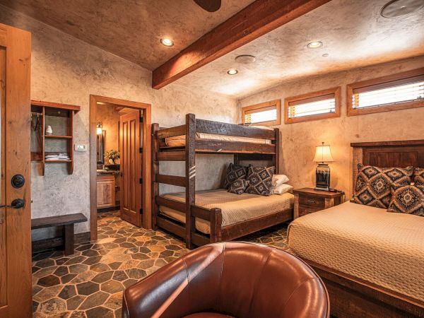 A cozy bedroom with a bunk bed, a double bed, stone flooring, wooden furniture, a warm color scheme, and rustic decor elements.