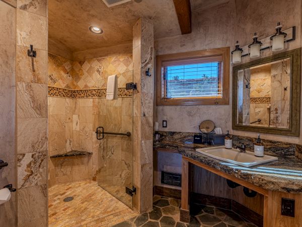 The image shows a luxurious bathroom with a walk-in shower, granite countertops, a large mirror, and wood accents, creating a rustic feel.